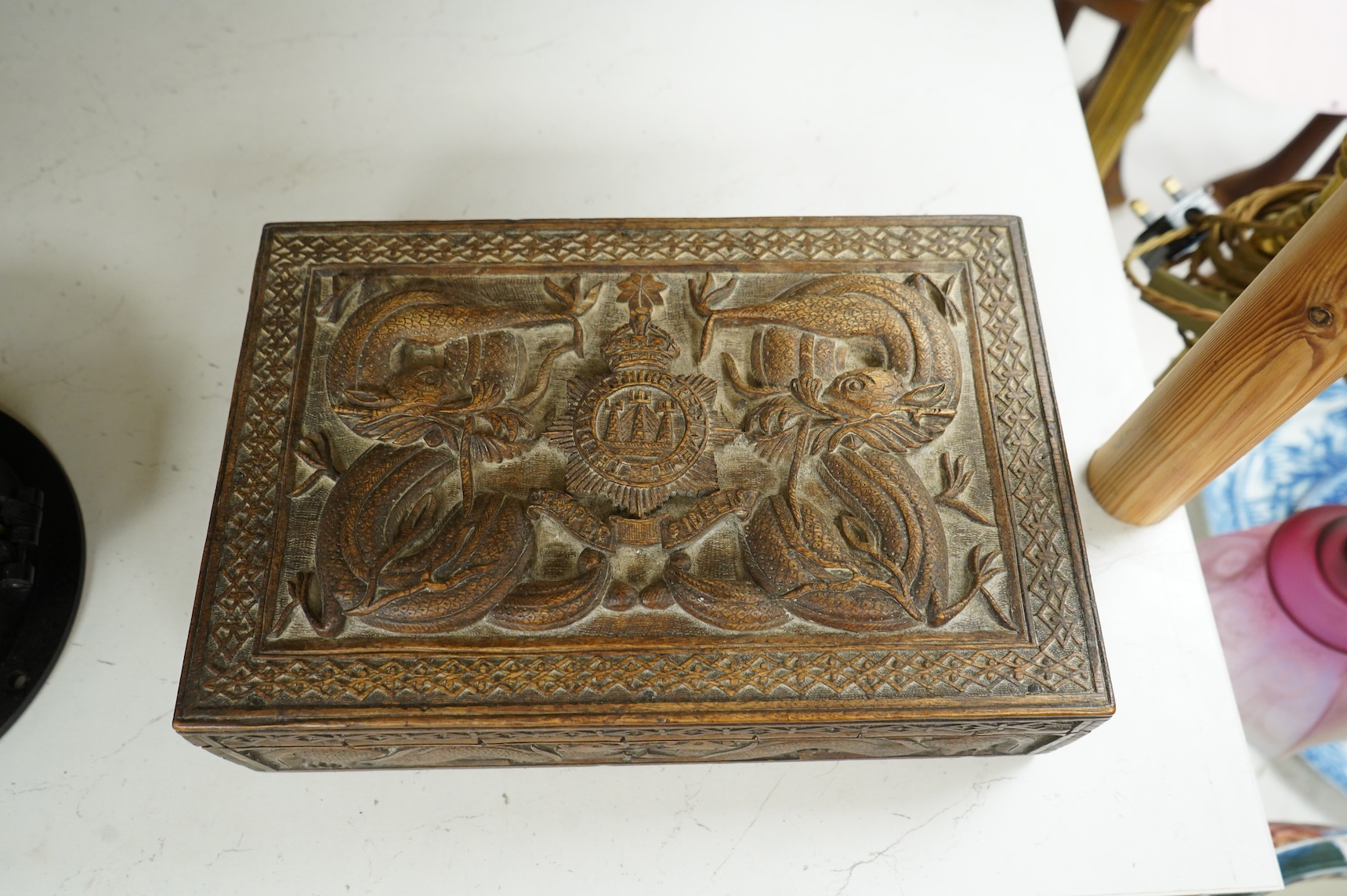A Burmese military themed carved box, early 20th century, heavily carved with the insignia of the Devonshire Regiment to the lid, surrounded by mythical dolphins, serpents, and geometric patterns, with segmented interior